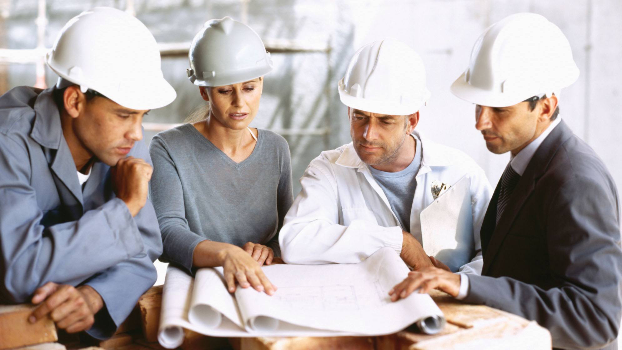 project engineer in a meeting with other project engineers standing around reading a piping and instrument diagram.