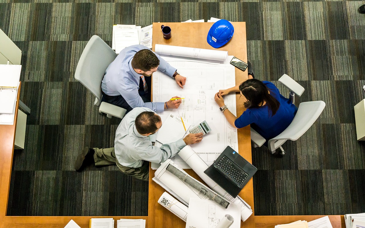 Three engineers seen from above, looking at blueprints on a desk
