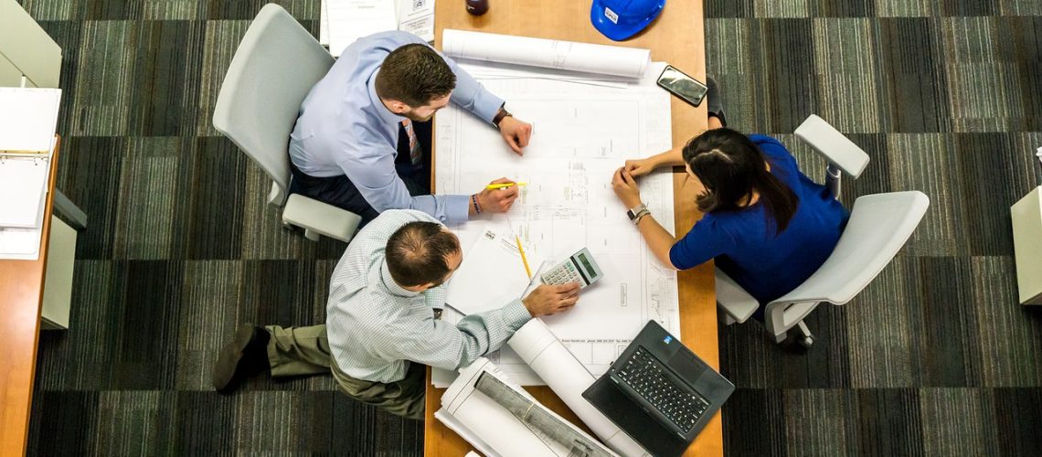 Three engineers seen from above, looking at blueprints on a desk