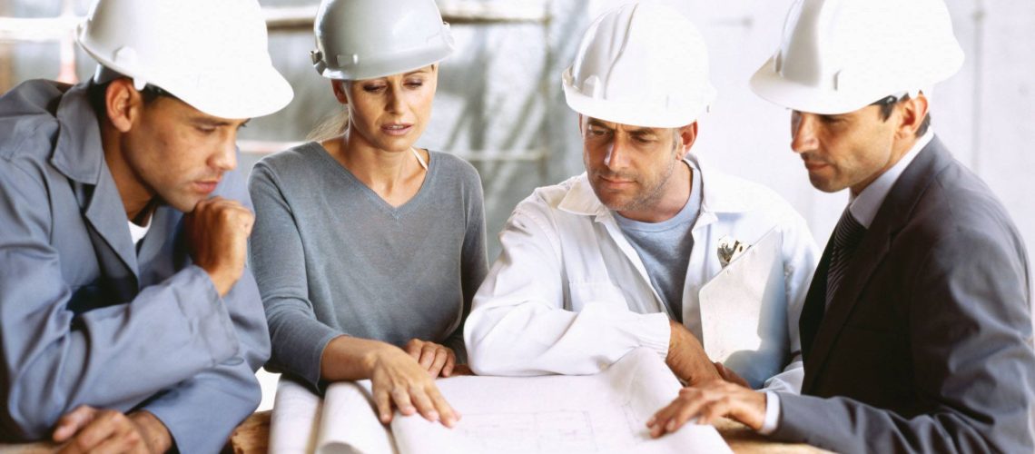project engineer in a meeting with other project engineers standing around reading a piping and instrument diagram.