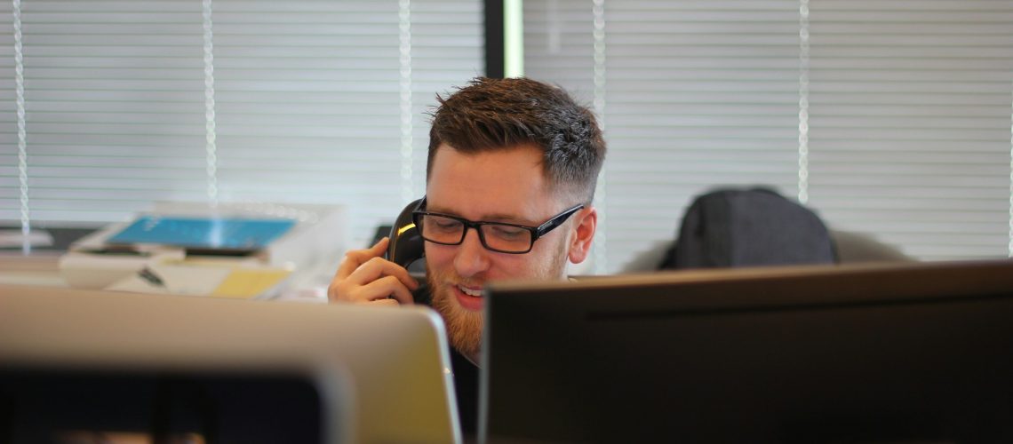 a quality control manager sitting behind two computer screens and holding a telephone.