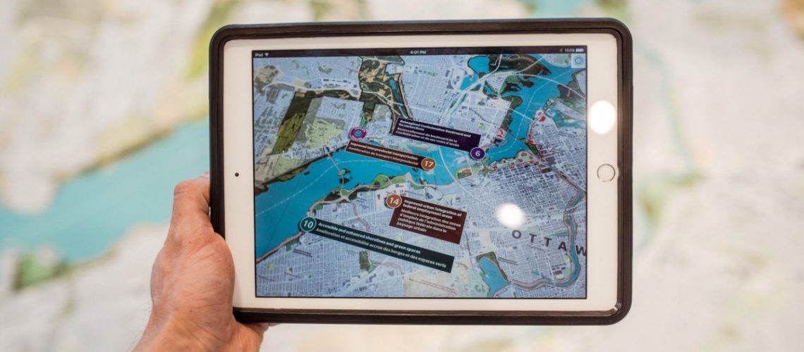 A hand holding a tablet displaying a virtual design of a building.