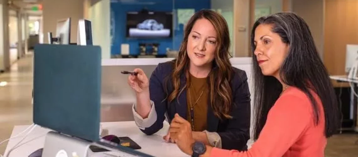 Two professional women discuss something while looking at a laptop